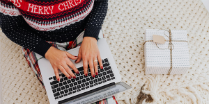 Overhead view of person wearing a Christmas jumper sitting with laptop on their lap. A present is sitting next to them.